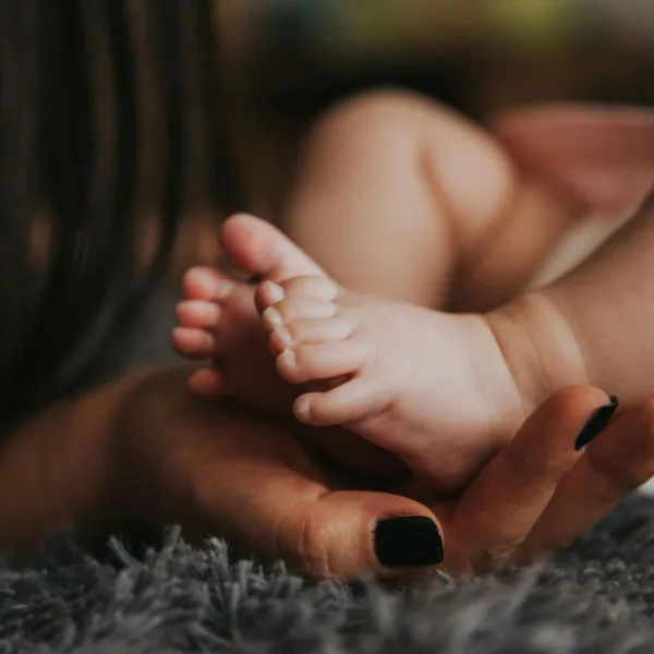 Mother cradling newborn baby's feet during postpartum recovery